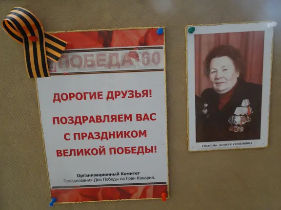 Cartel con lazo S. Jorge, Ryazanova Semenova, heroína en contraespionaje, retirada en esta isla y Felicitación: "Estimados amigos les felicitamos por la Fiesta de la Victoria".